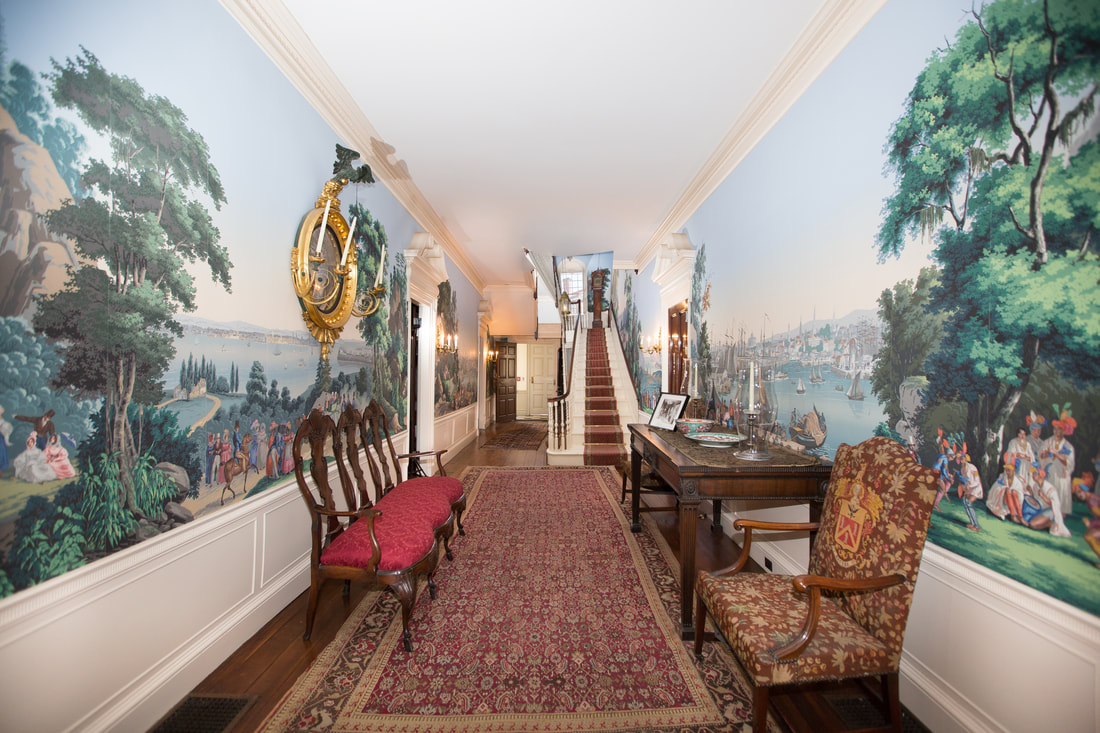 Interior hallway with view up the stairs, armchairs on either side, decorative rugs, and wallpaper with panoramic imagery.